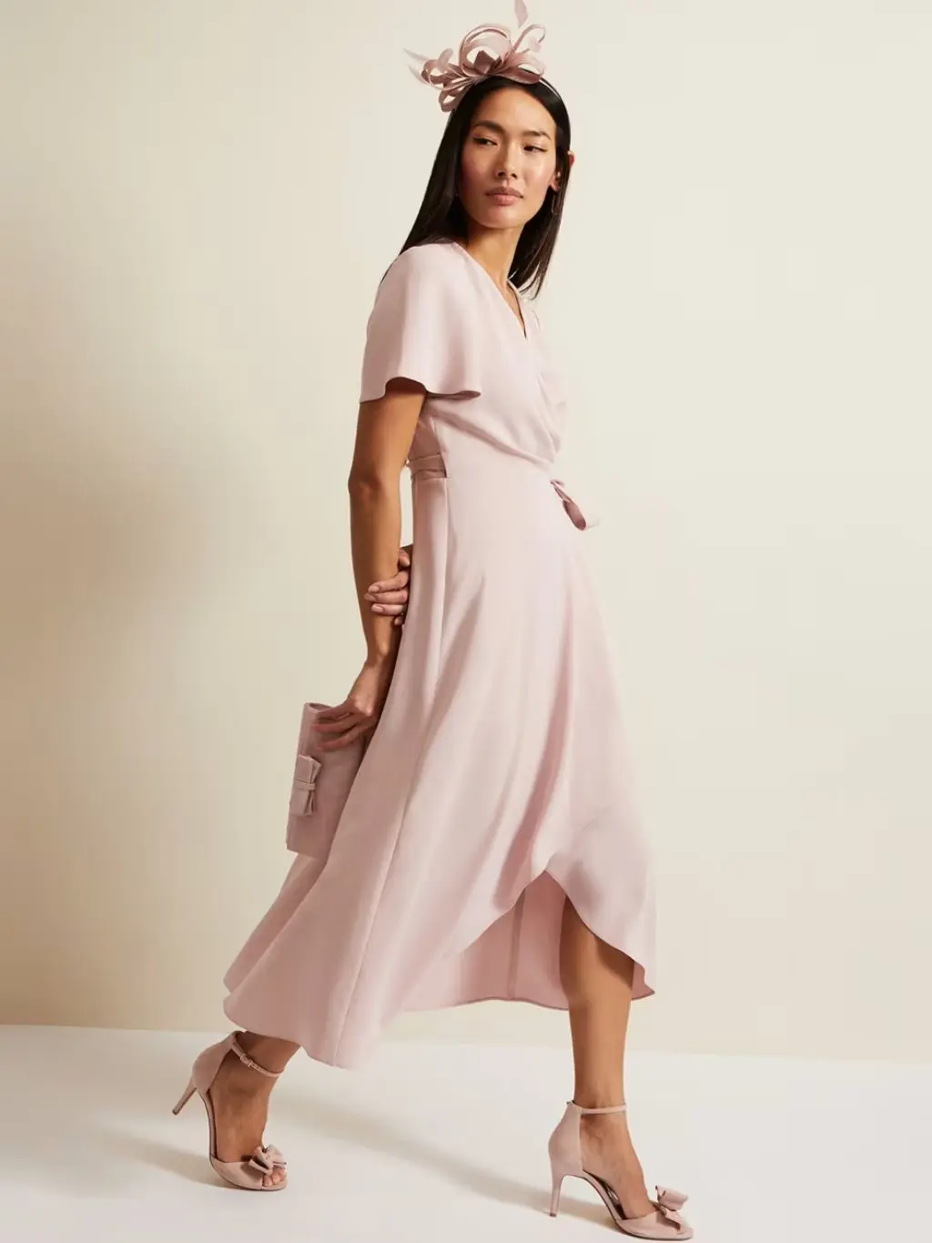 Woman wearing a pale pink Phase Eight wrap dress, fascinator and heels