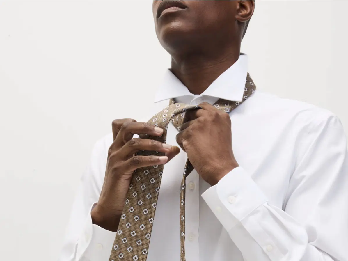 Man wearing white shirt and tying a brown patterned tie