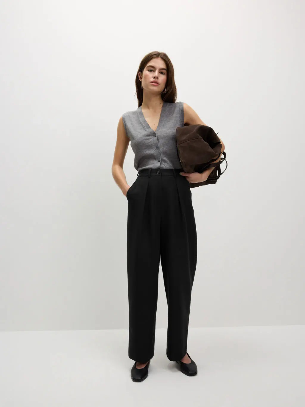 Woman wearing black trousers with a grey knitted vest, black pumps and a black tote bag.