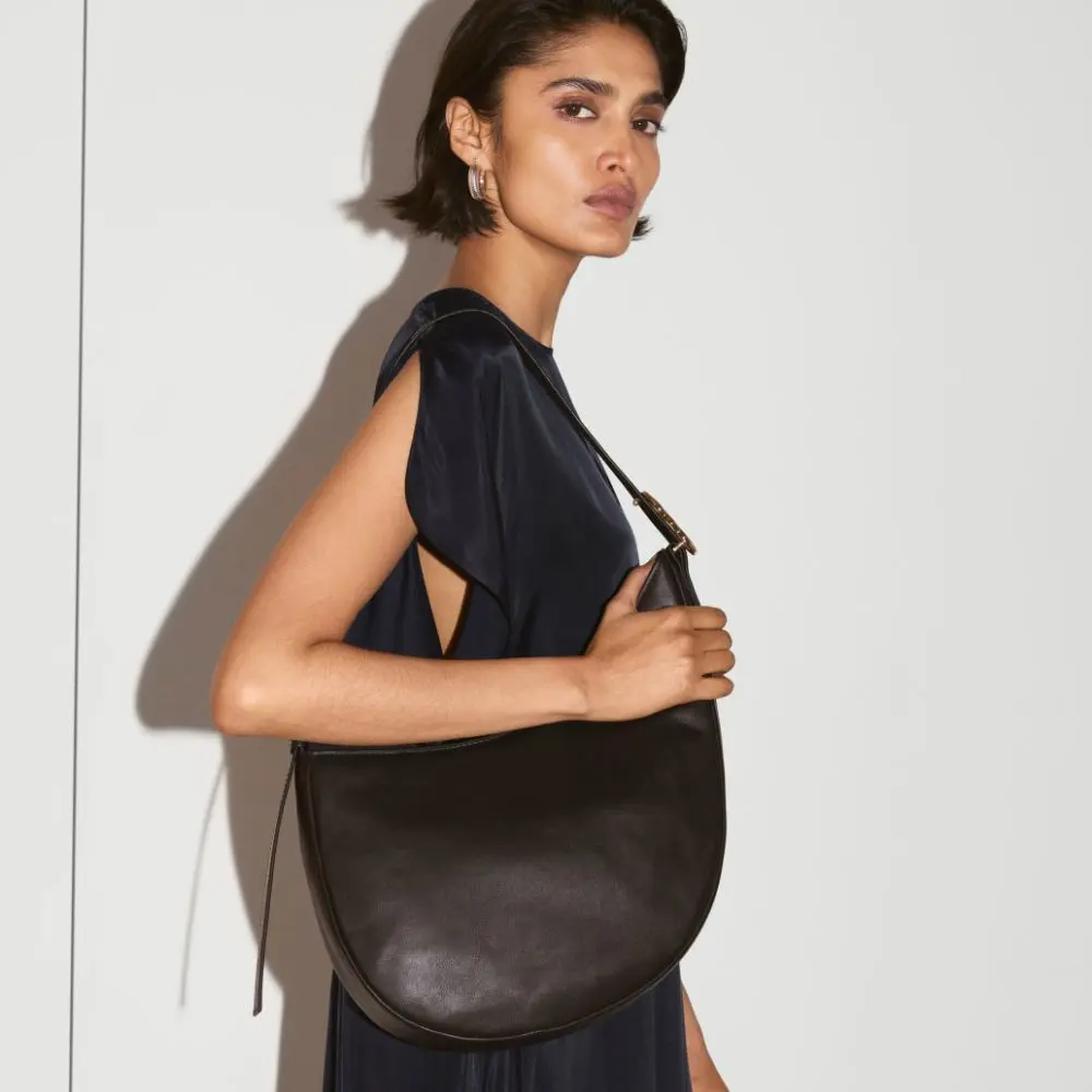 A woman carries a half moon handbag over her shoulder