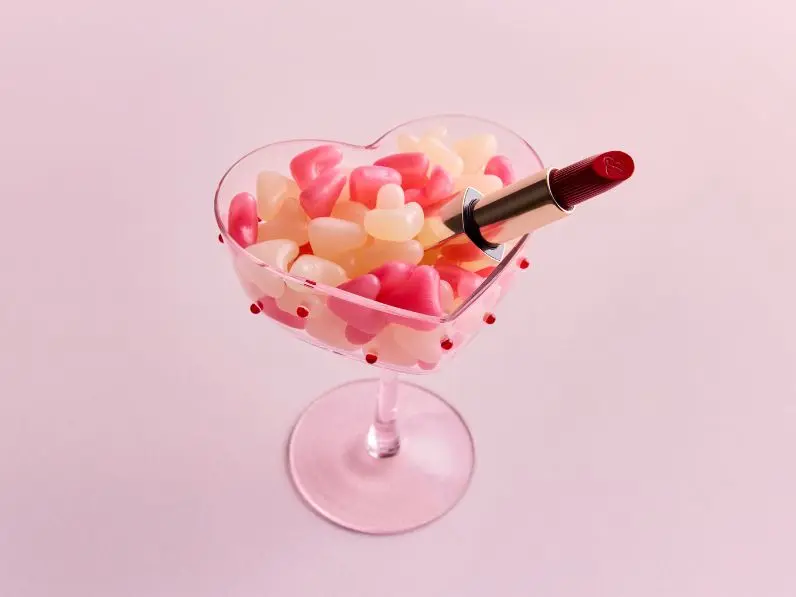 A heart shaped coupe glass filled with jellybeans and a red lipstick