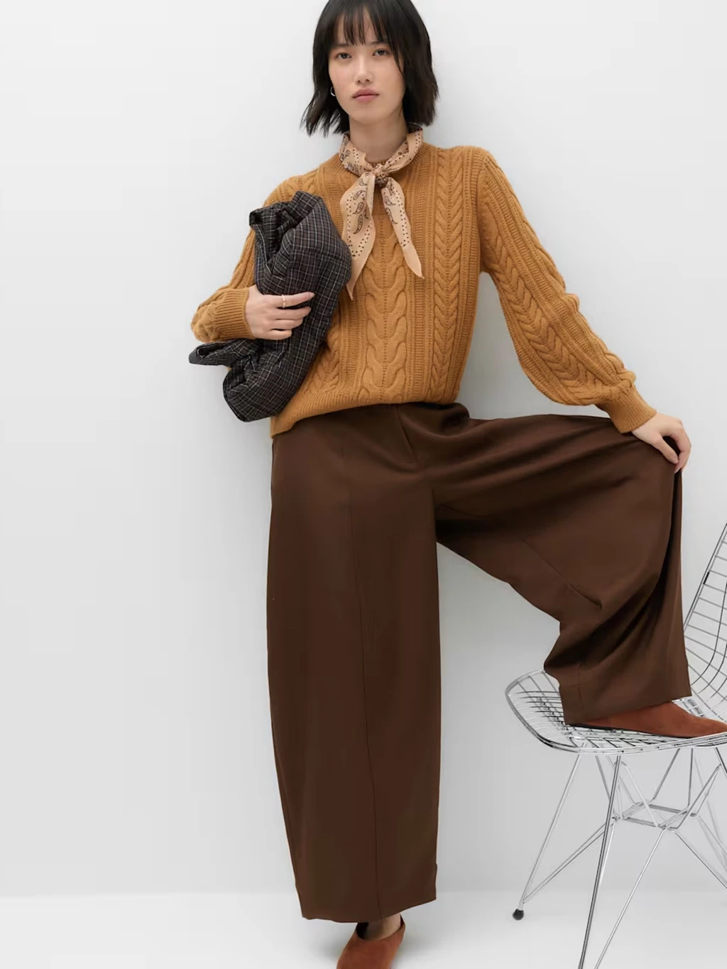 Woman wearing brown trousers with a burnt orange cable knit jumper.