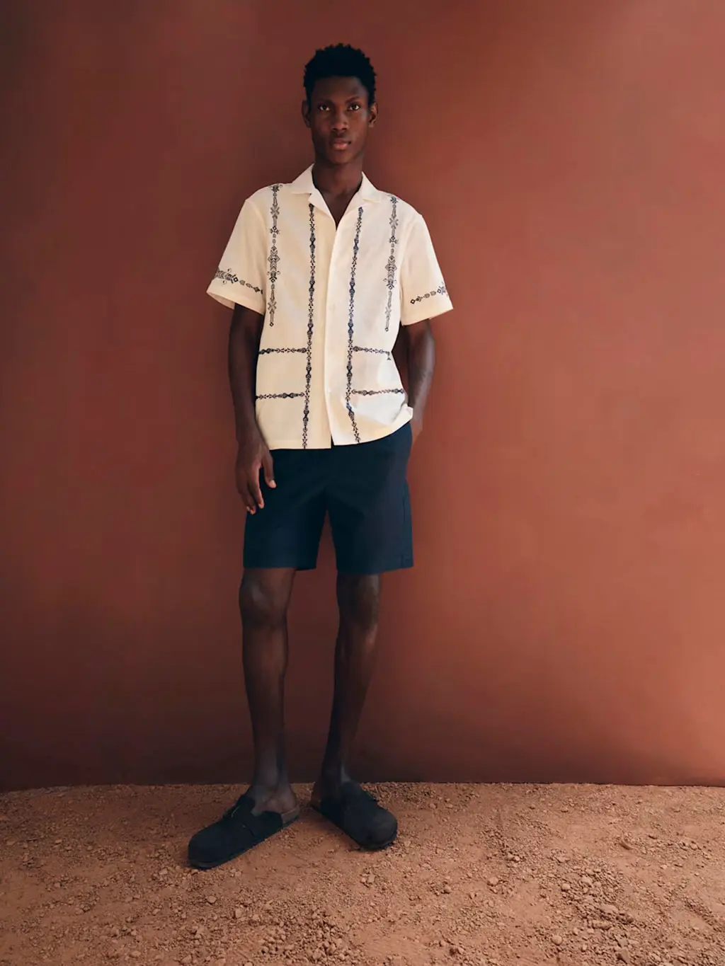 Man wearing a embroidered linen shirt with navy shorts and clogs