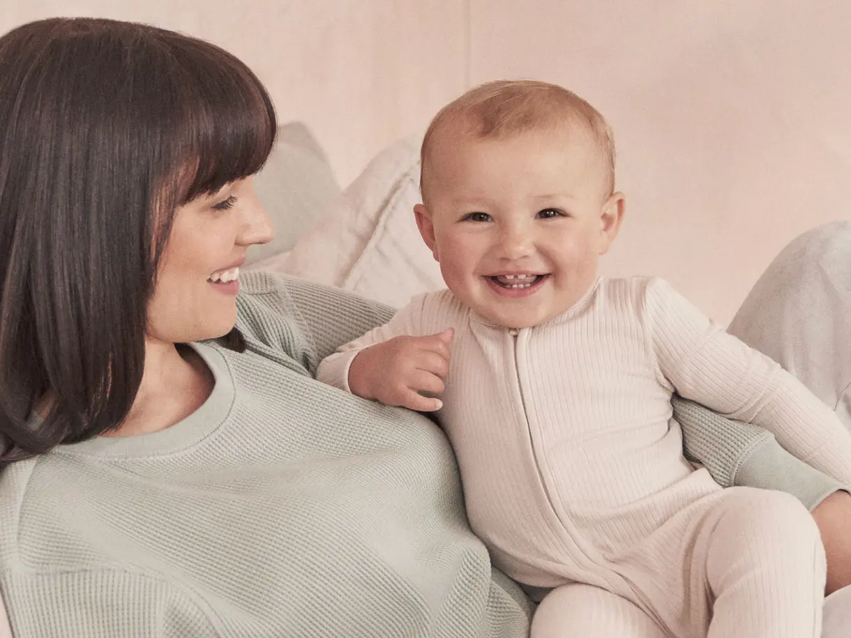 Brunette woman holding smiling baby in neutral sleepsuit