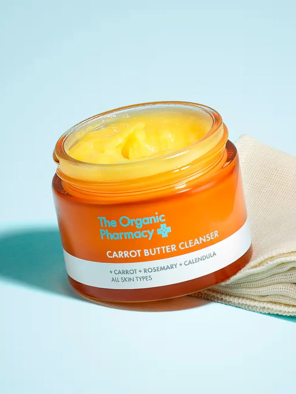 A jar of The Organic Pharmacy Carrot Butter Cleanser is opened and shot against a blue background