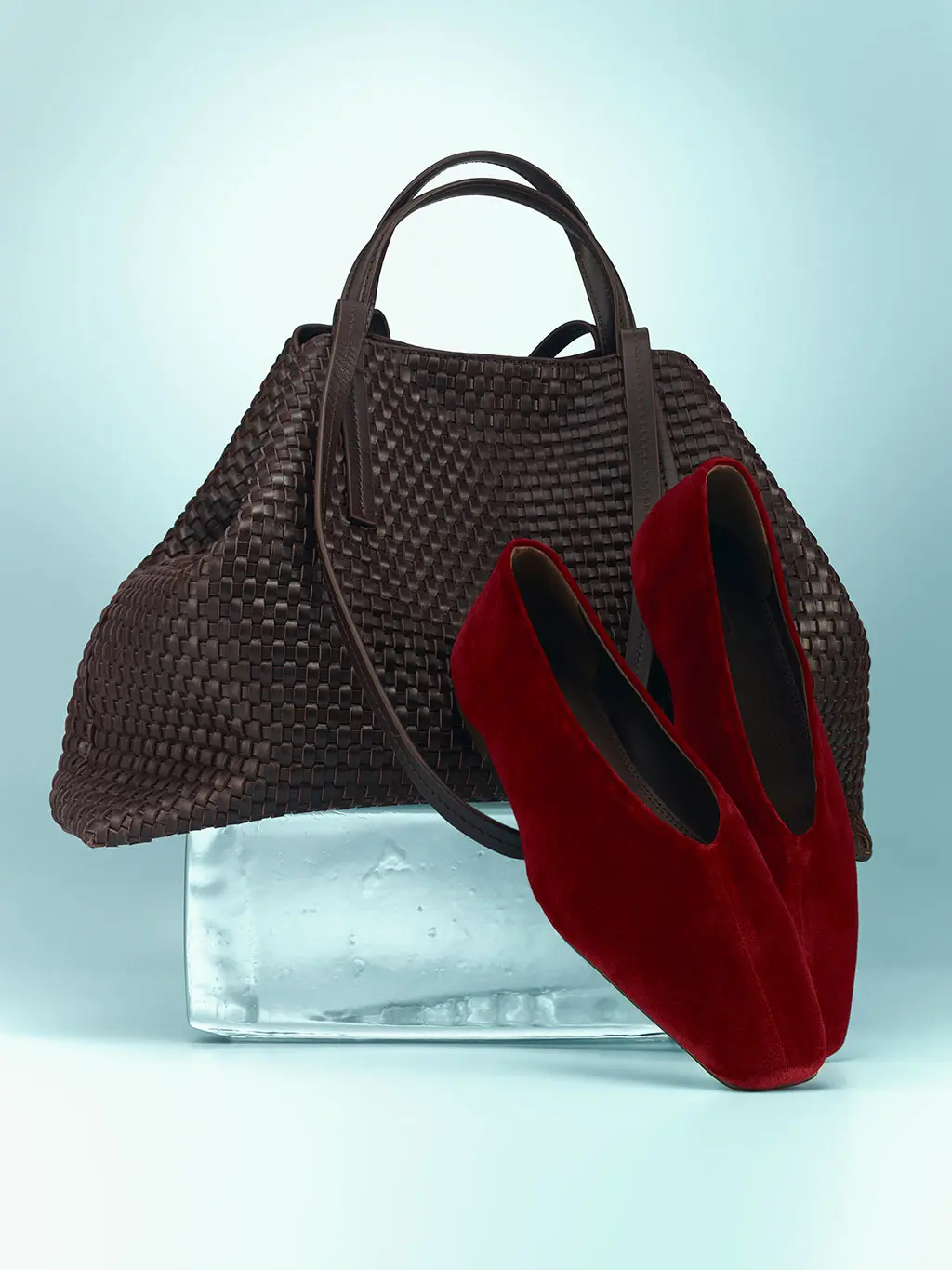 Brown bag with a woven surface and red suede ballet flats.