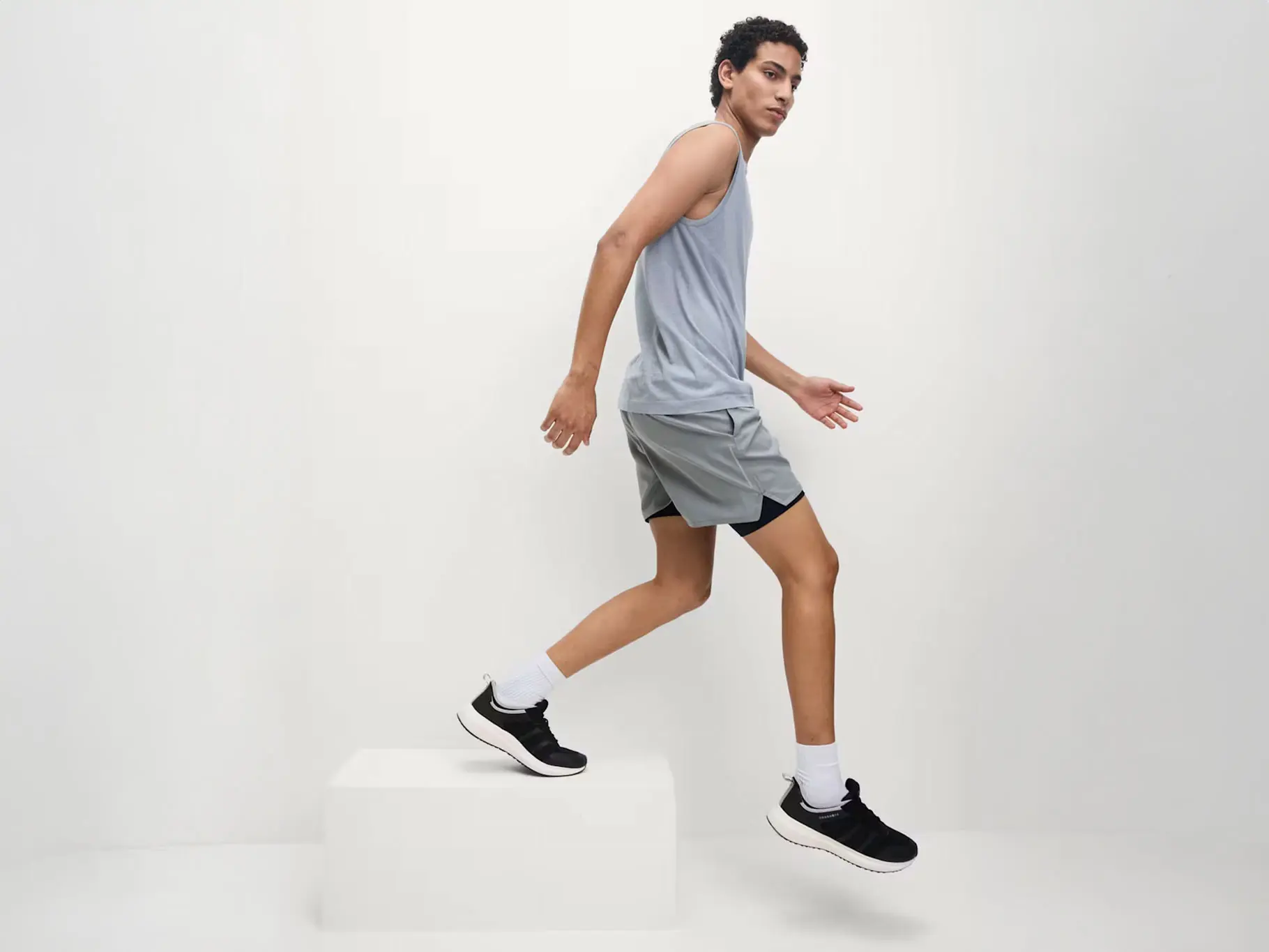 Man wearing a grey vest with shorts and black trainers
