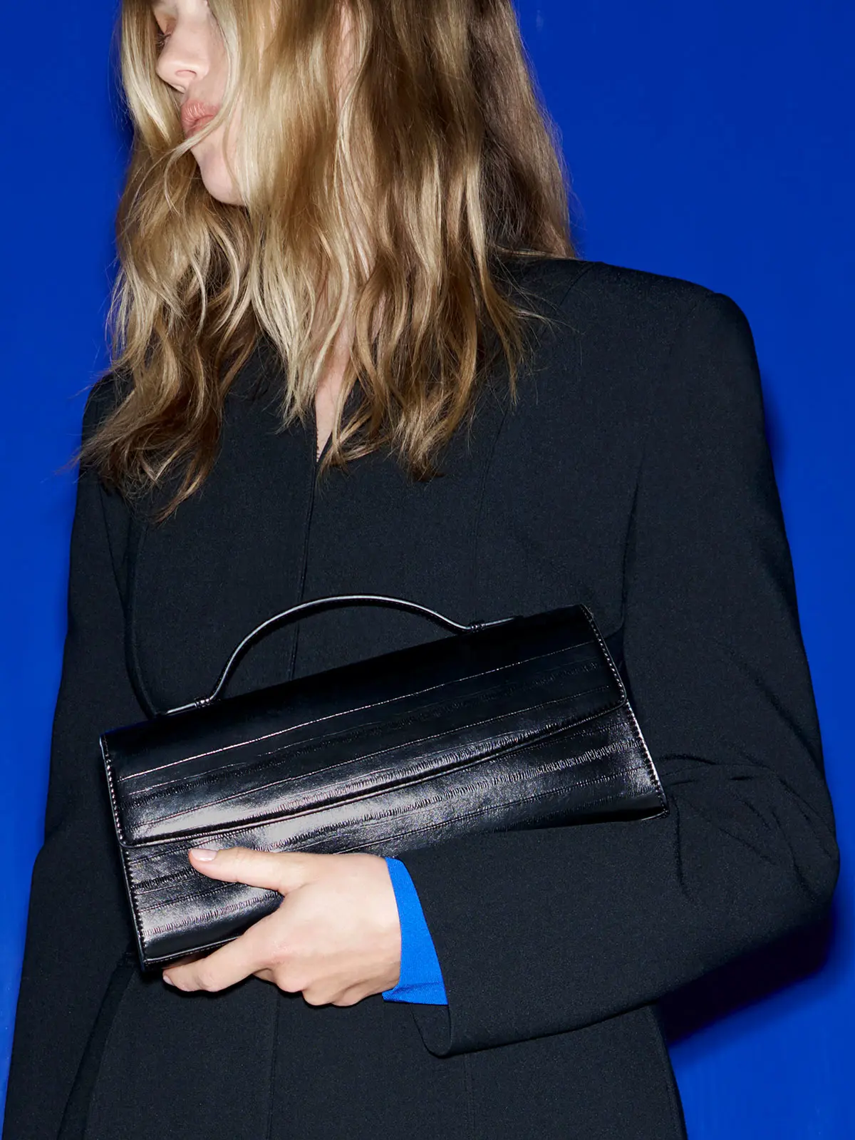Woman wearing black blazer over blue blouse and holding black bag