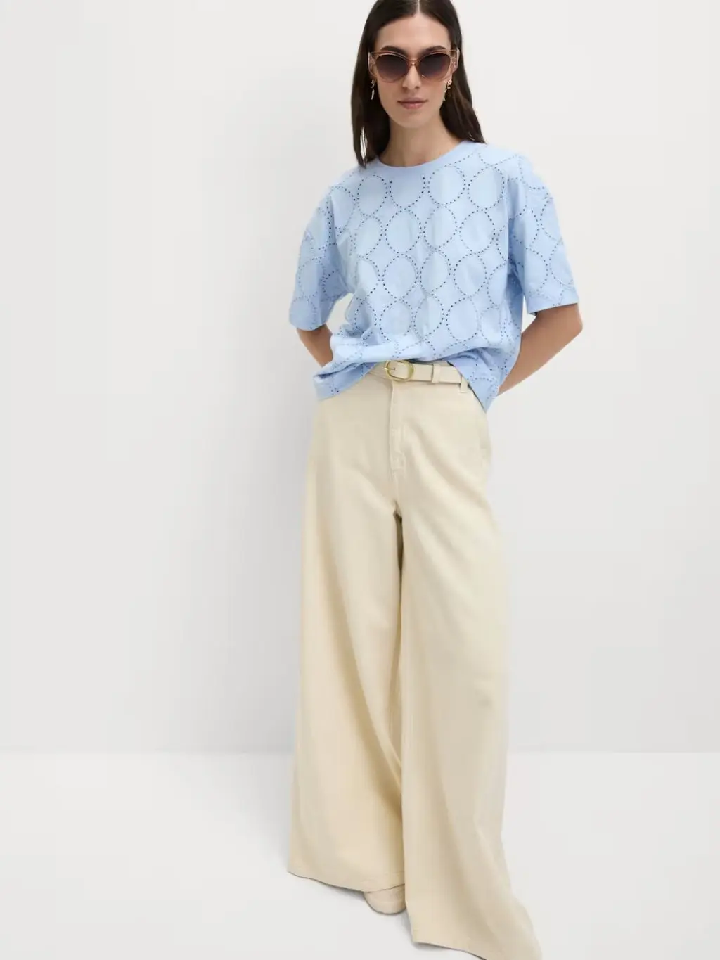 A woman wears a pale blue top with wide leg cream jeans