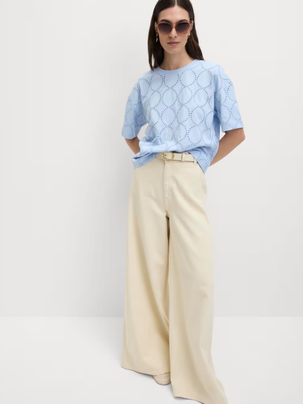 A woman wears a pale blue top with wide leg cream jeans