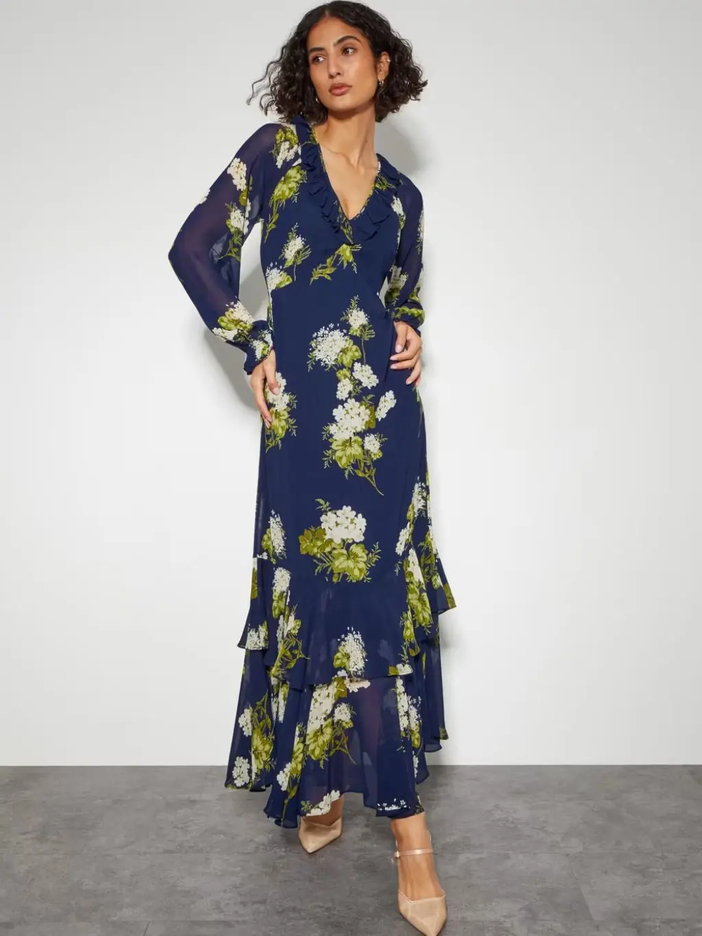 Woman wearing a long floral navy and cream chiffon ruffle dress from Monsoon