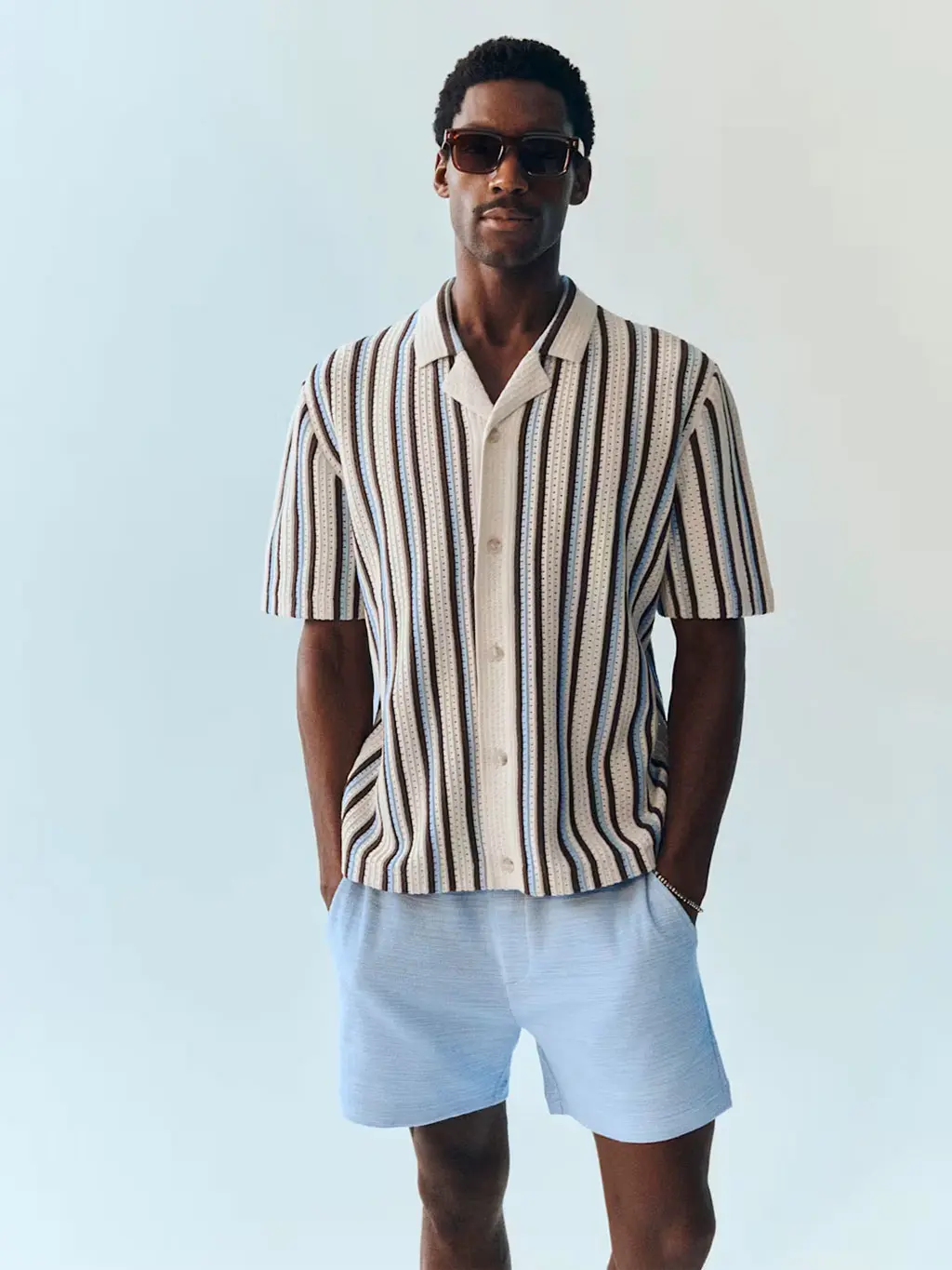 Man wearing a striped knitted polo shirt with blue shorts