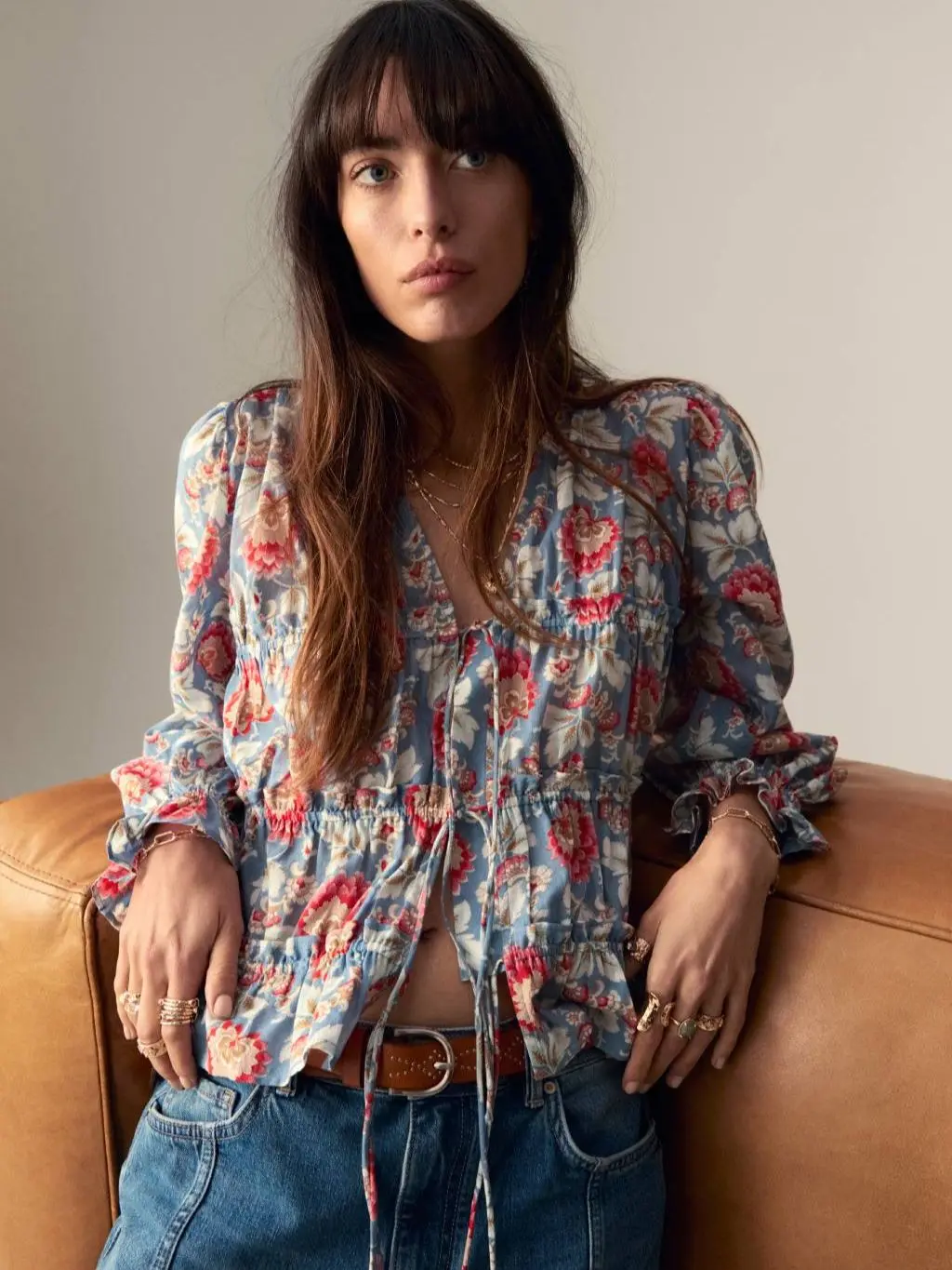 A woman wears a floral tie front blouse with blue jeans