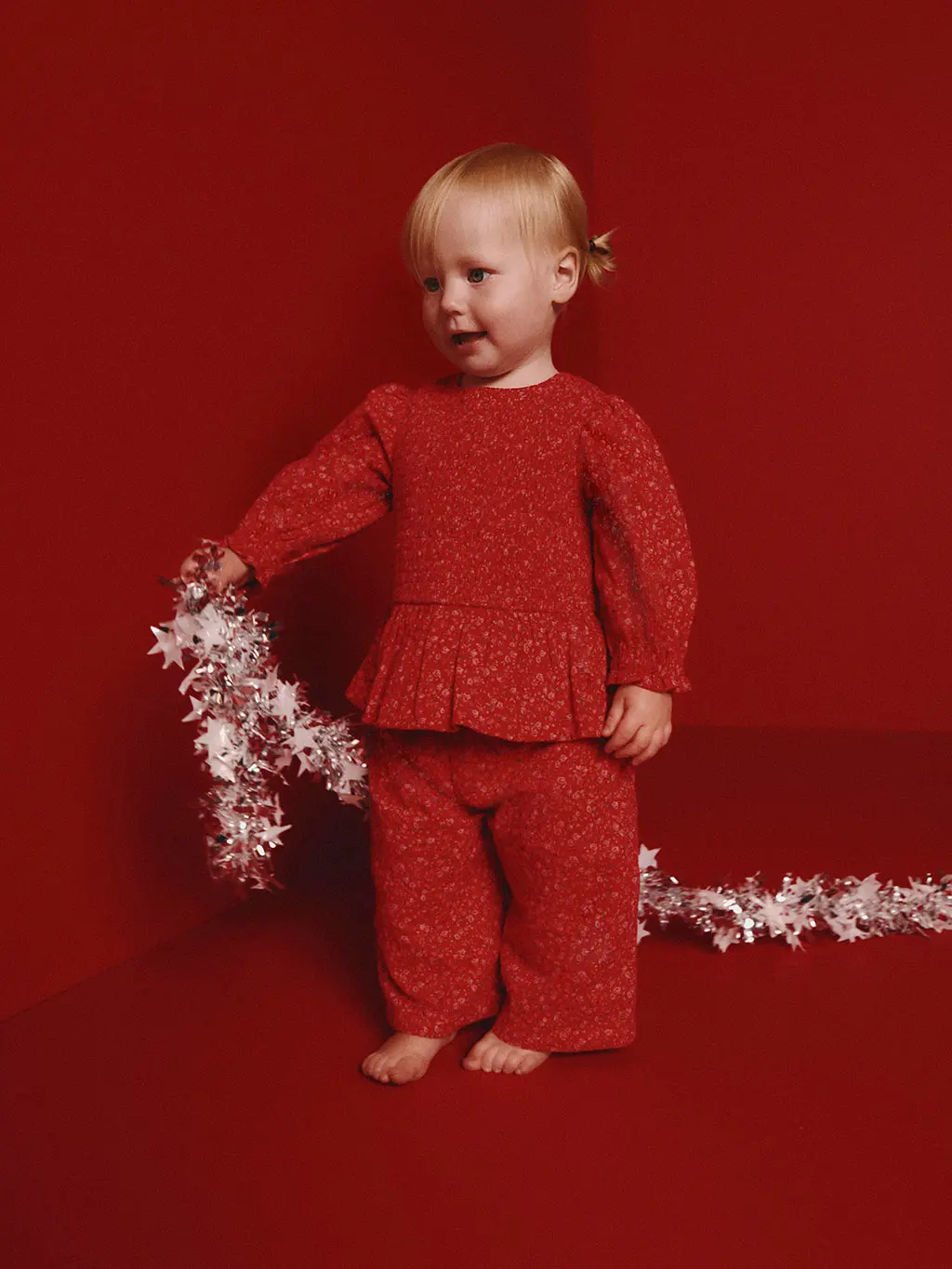 Young girl in a matching set of red pyjamas holding some tinsel.