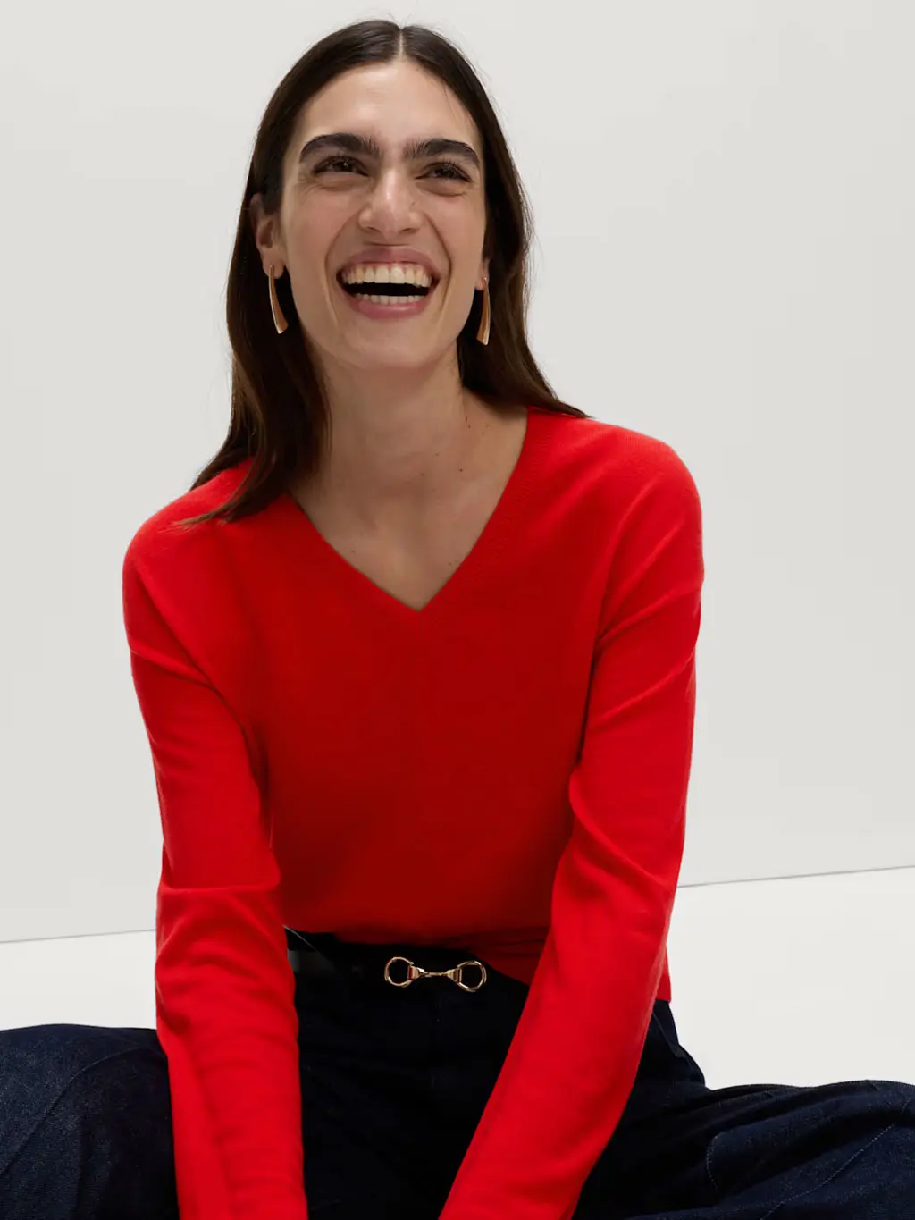 Woman wearing a red V-neck jumper with a indigo-blue jeans and a black belt with gold hardware