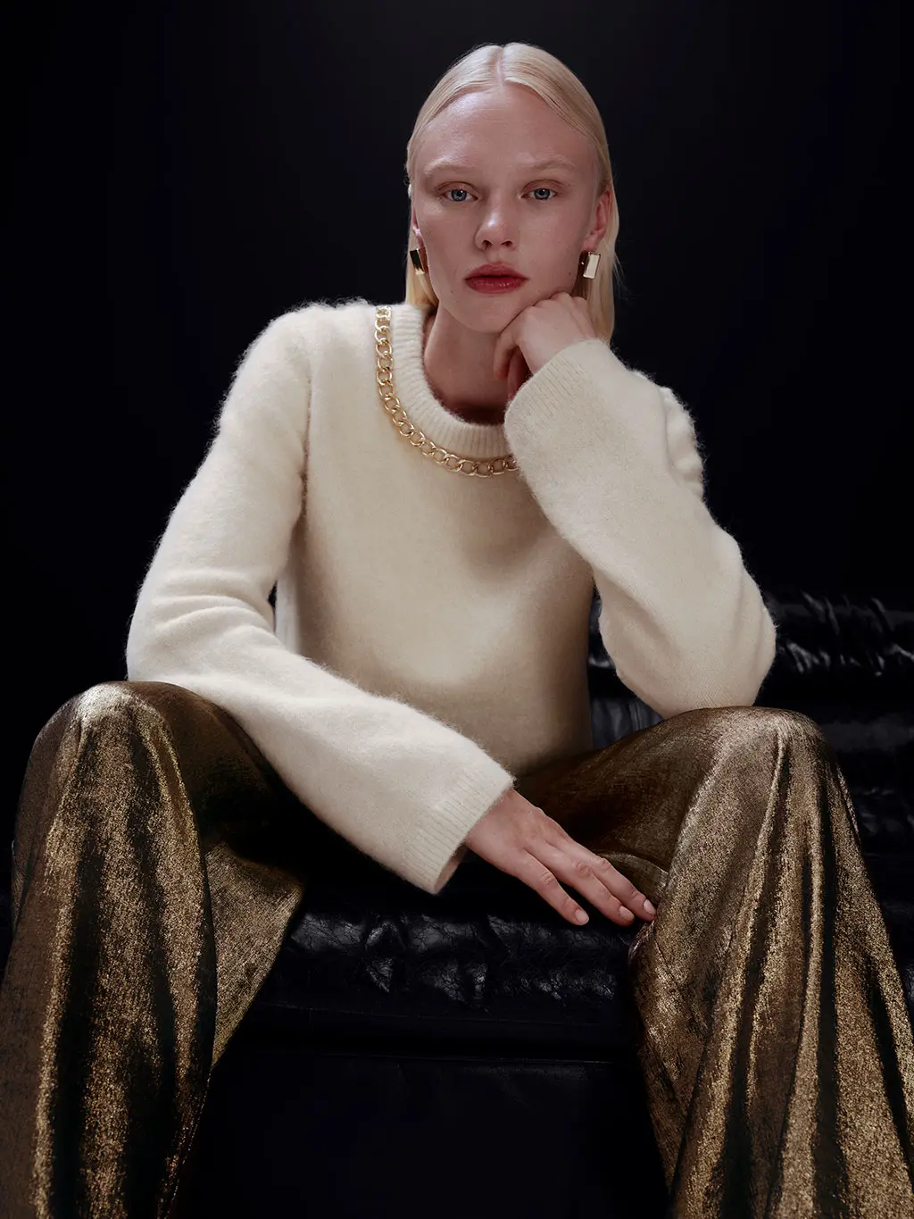 Woman wearing an embellished white jumper with gold glittery trousers and gold hoop earrings.
