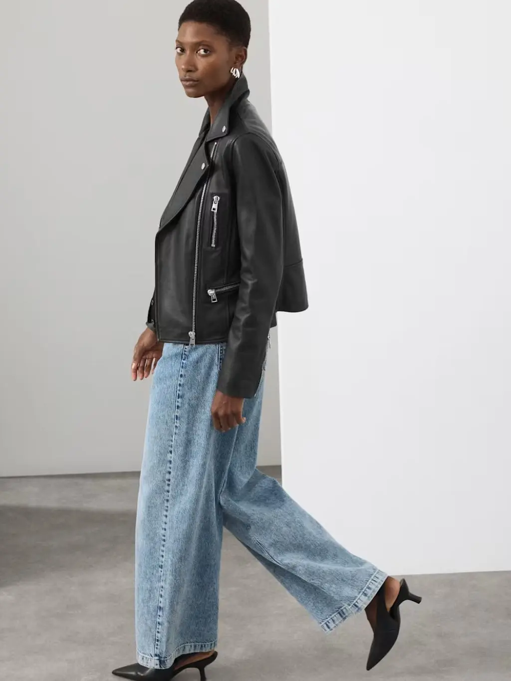 A woman wearing a leather biker jacket, barrel leg jeans and slingback heels