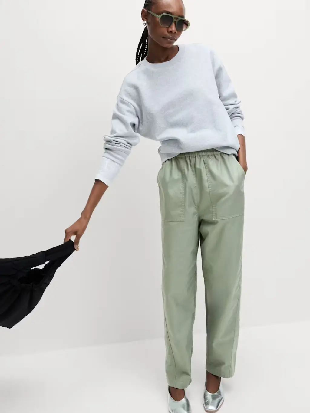 A woman wears a grey sweatshirt and pale green trousers, while carrying a black handbag