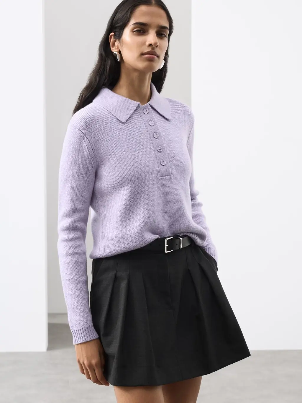 A woman wears a lilac knitted polo shirt and a black mini skirt with a buckle belt