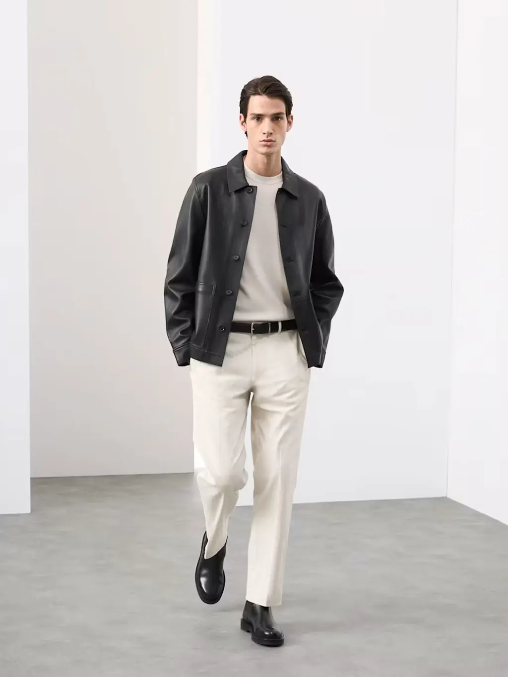 Man wearing a white top and trousers with a black leather jacket, belt and Chelsea boots