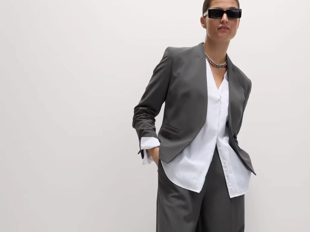Woman wearing grey collarless blazer, white shirt and grey trousers