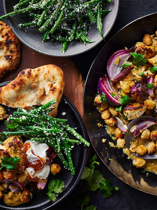 Bowls of curry, naan bread, ad green beans