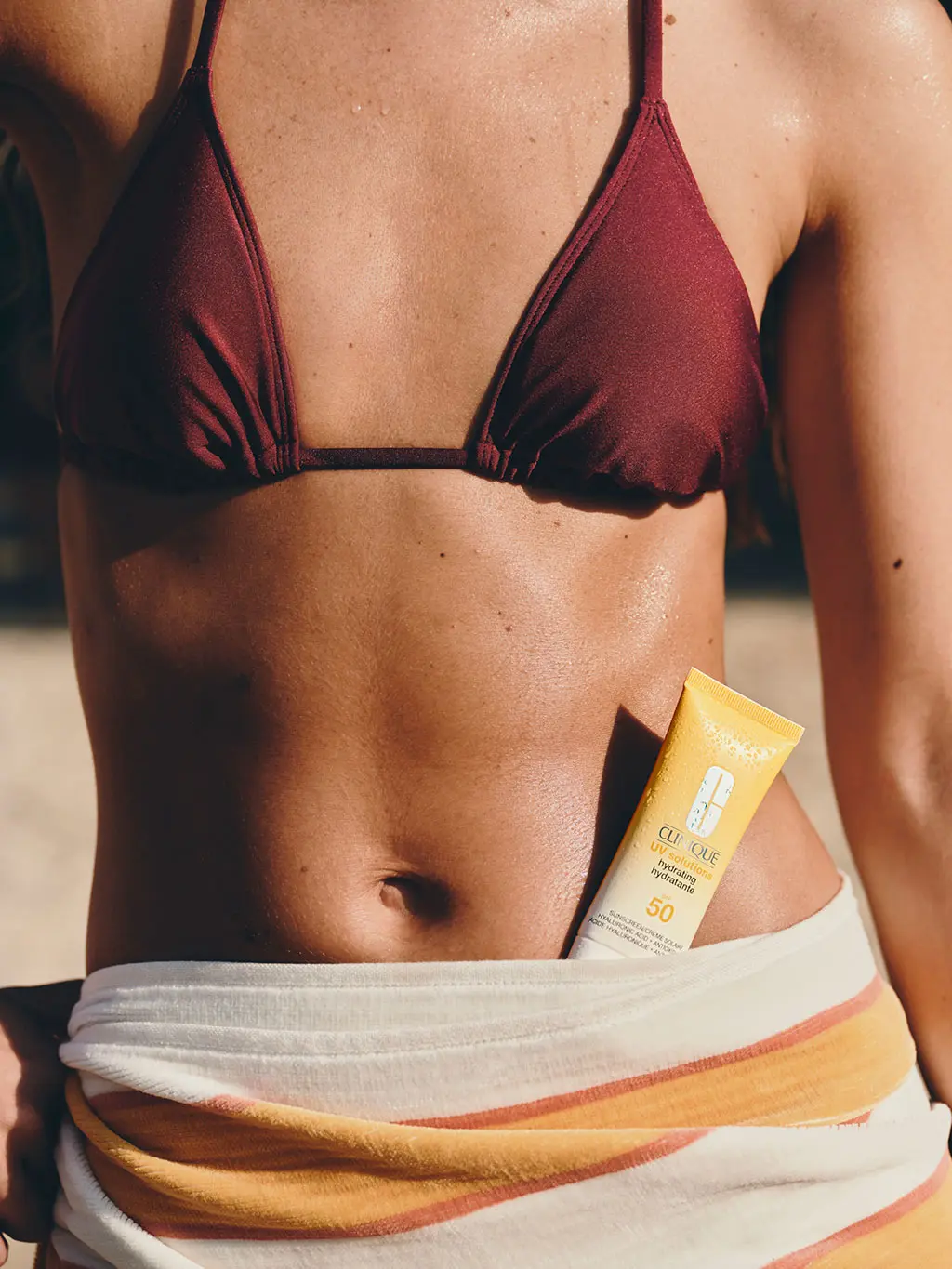 Woman in brown bikini with sunscreen tucked into waistline