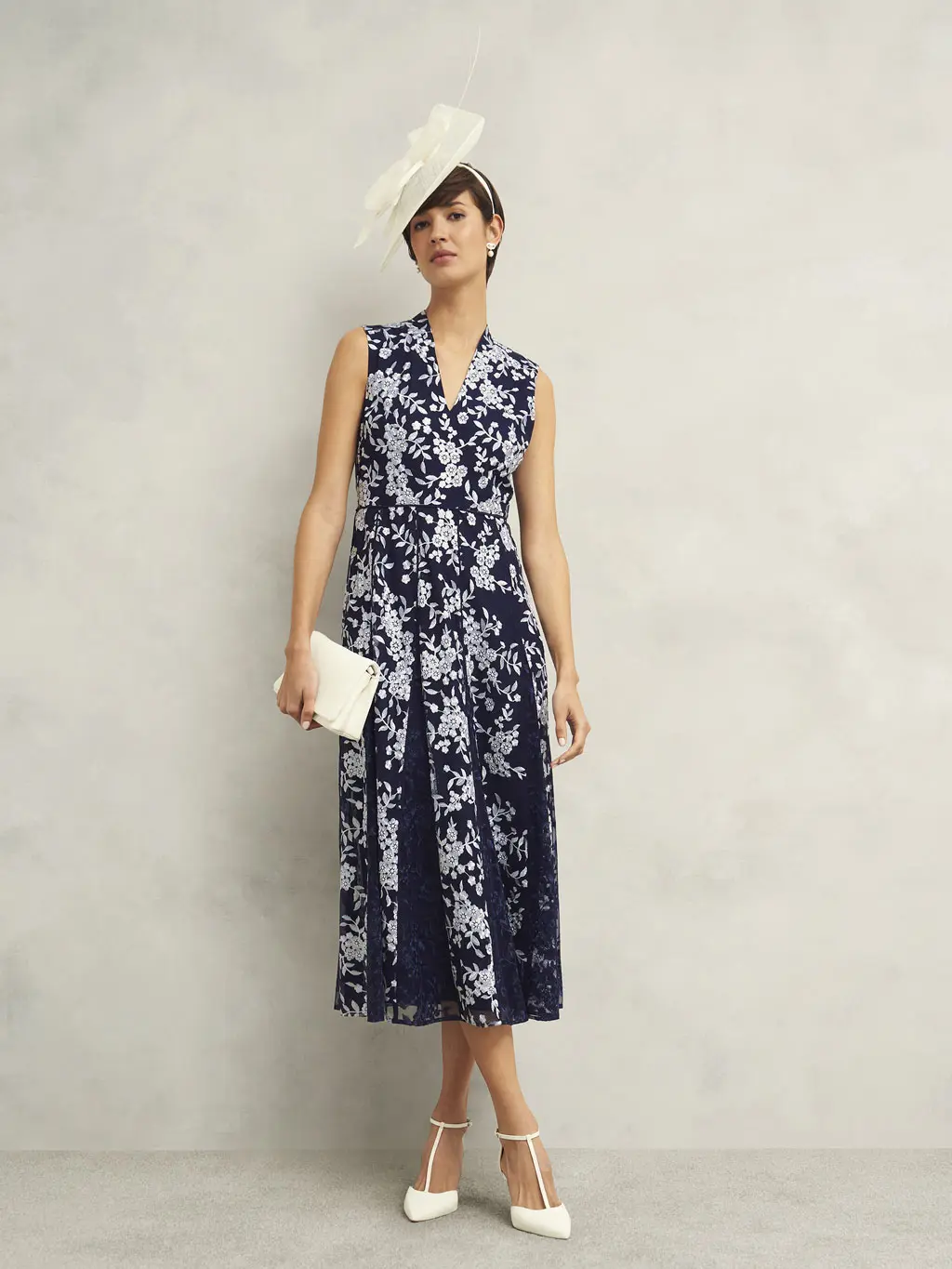 Woman wearing a navy floral-print dress, fascinator and white accessories 