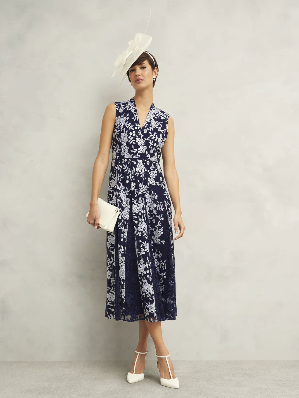 Woman wearing a navy floral-print dress, fascinator and white accessories