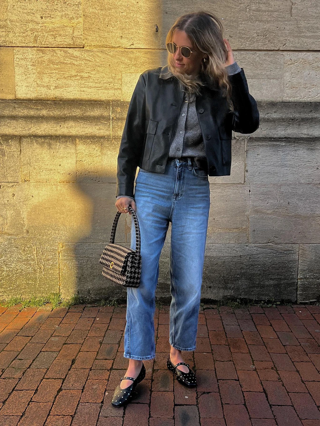 Prunella Poppy wearing black studded Mary Janes with a leather jacket and a pair of blue cropped jeans