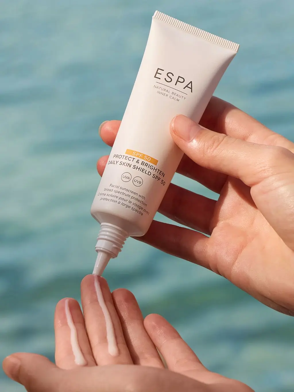 A woman puts ESPA suncream on her hands against the backdrop of the ocean