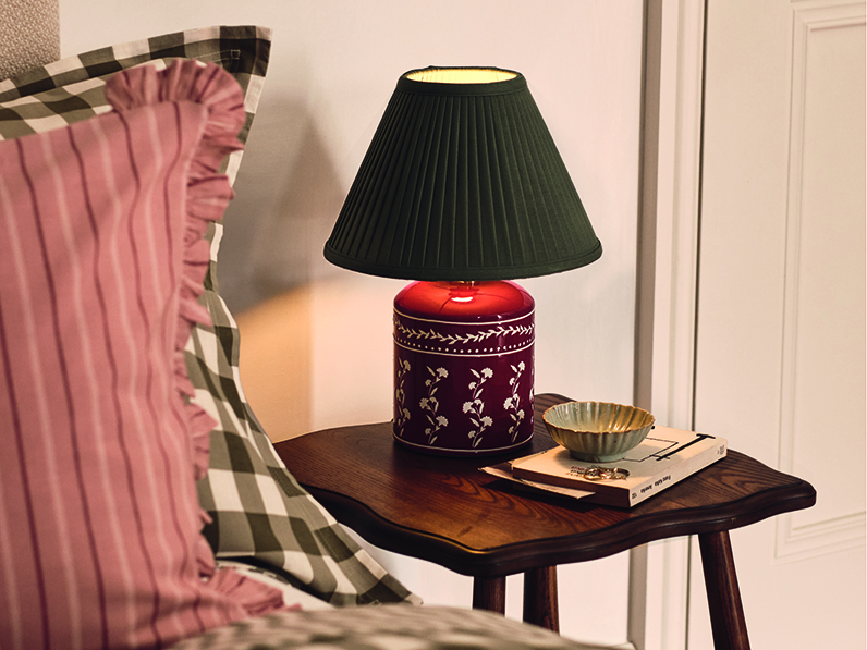 A green and orange ceramic lamp on a wooden bedside table