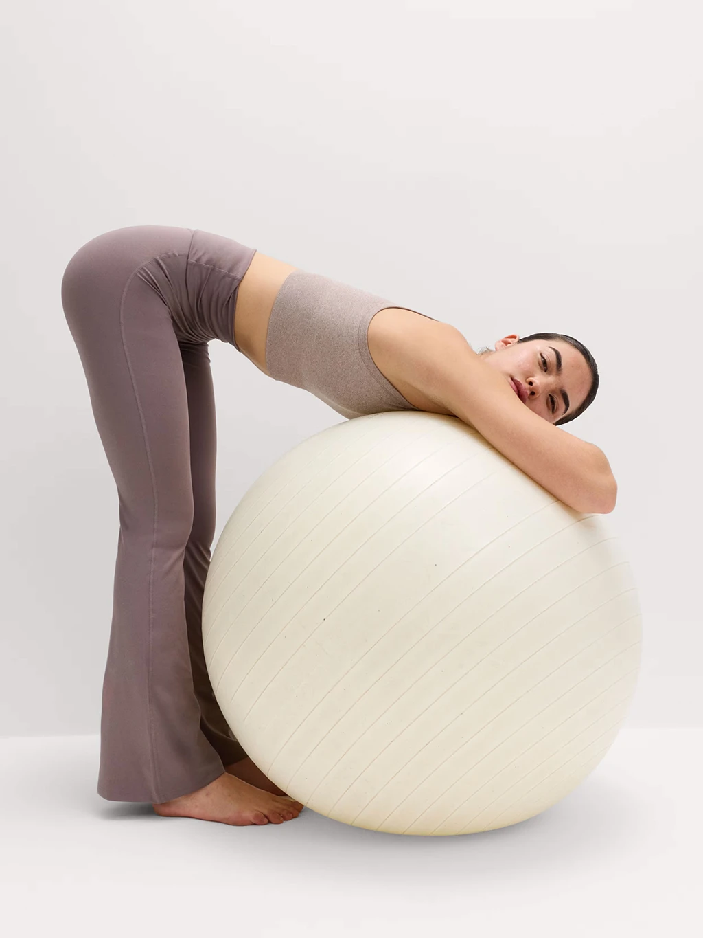 Woman wearing dusky pink sports bra and flared leggings using a cream sports ball