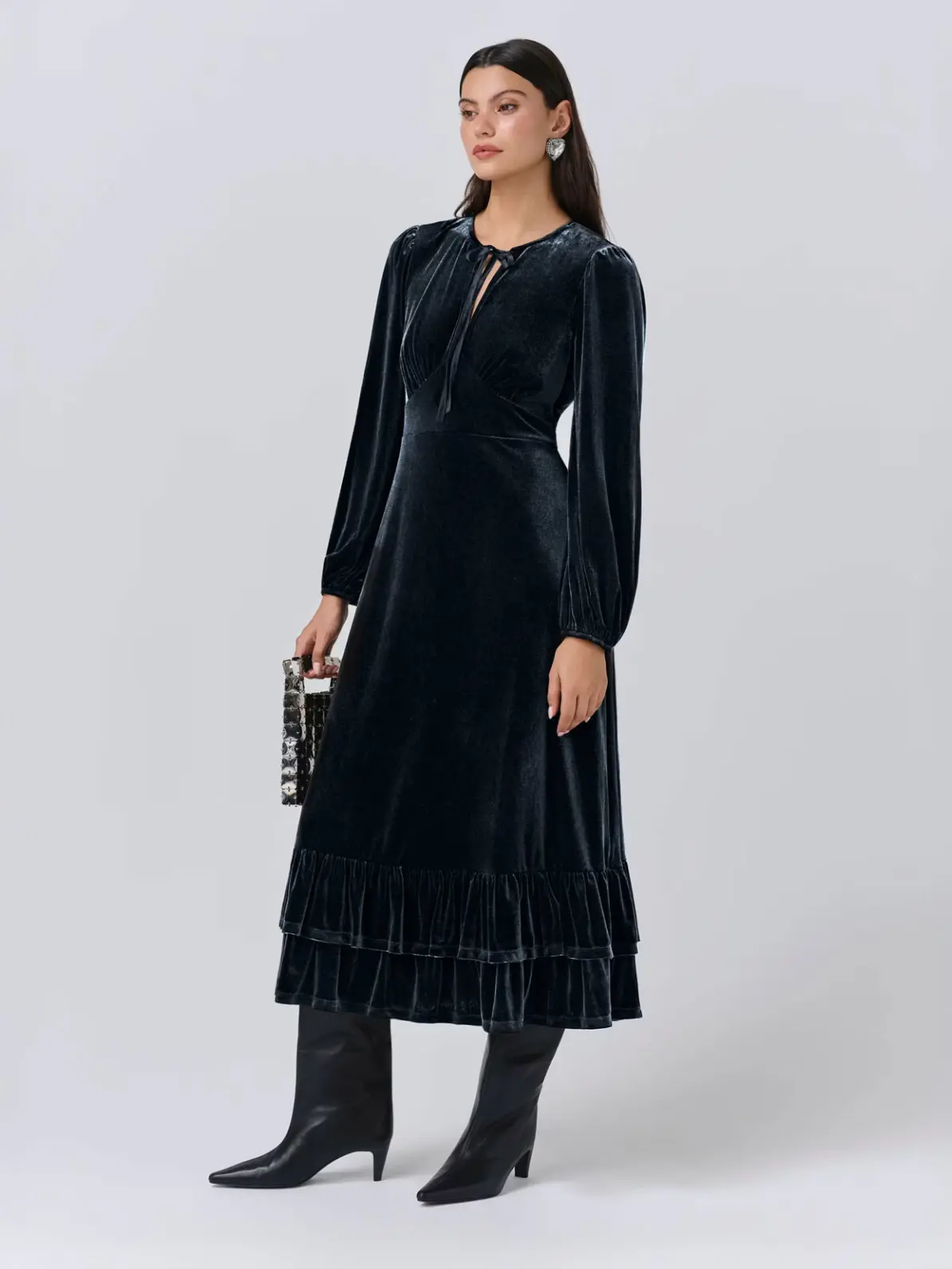 Woman wearing dark grey velvet dress with tall black boots and embellished clutch bag