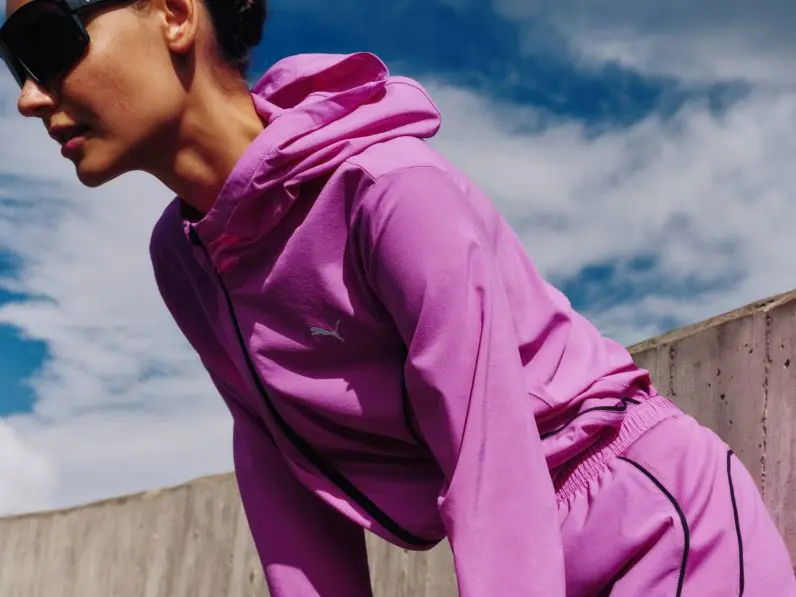 A woman wears bright pink Puma and tracksuit and shorts, while taking a rest from a run