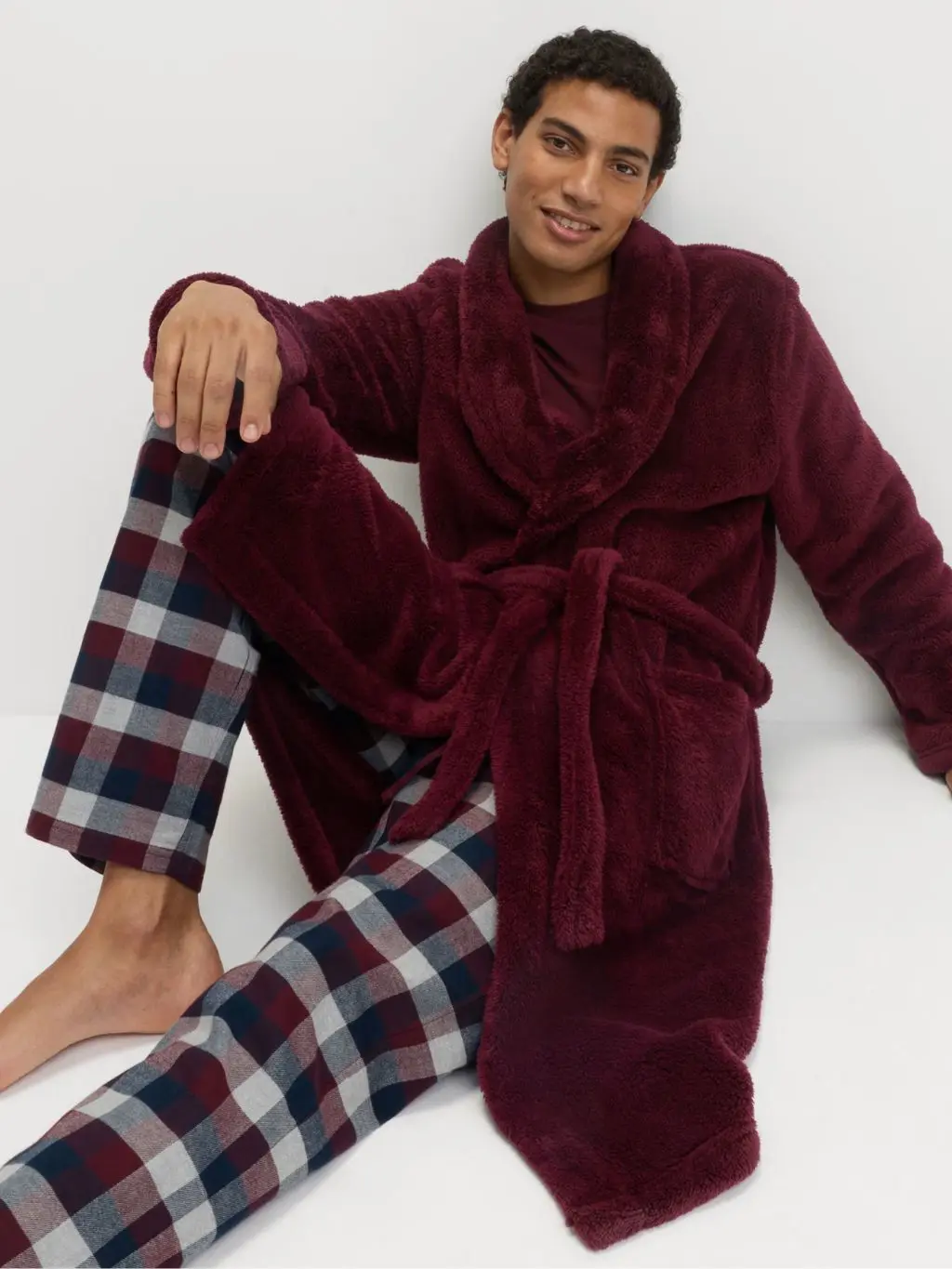 A man wears a burgundy dressing gown and matching check loungewear bottoms