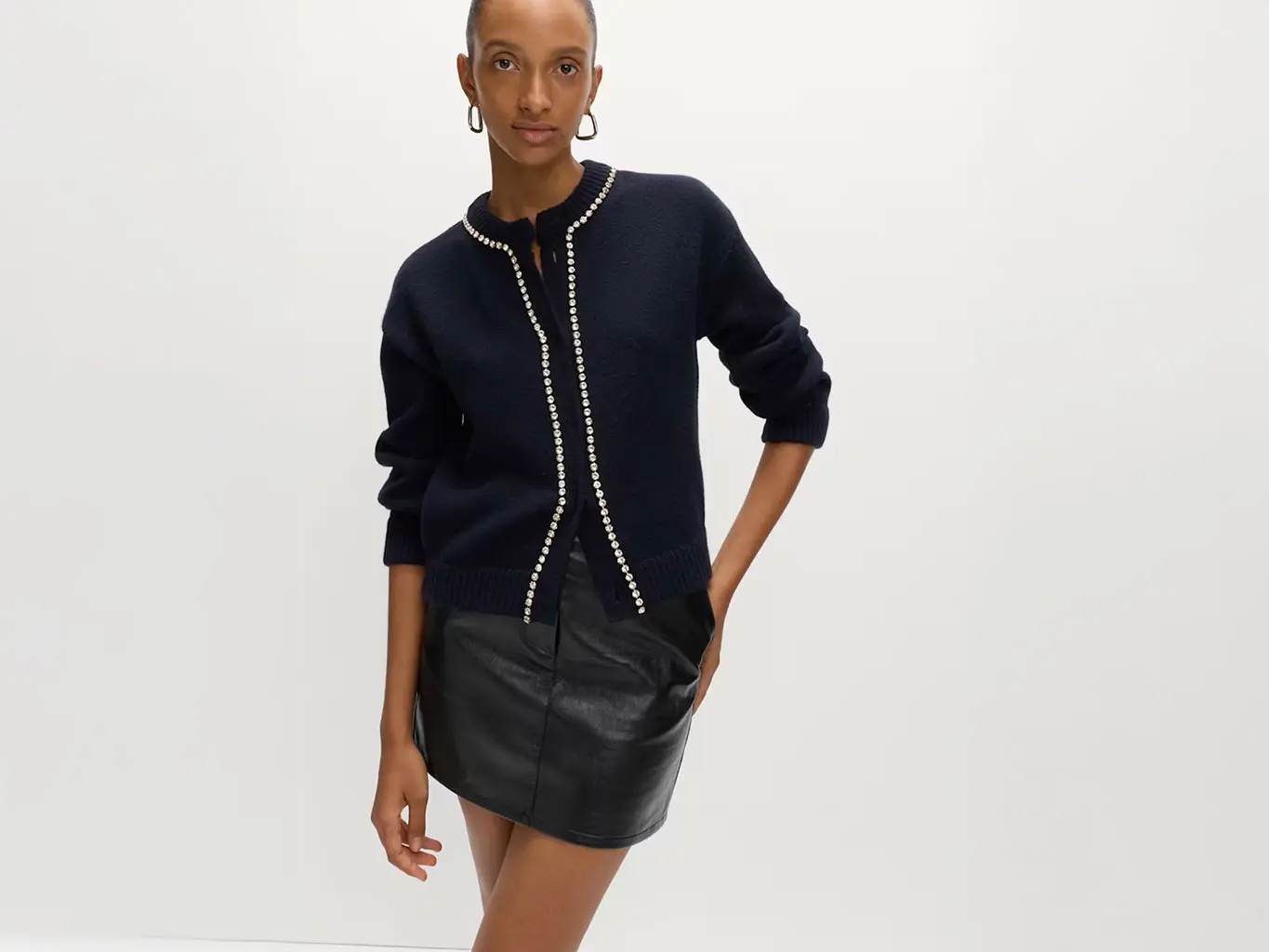 Woman wearing a black faux-leather mini skirt with a beaded cardigan and hoop earrings