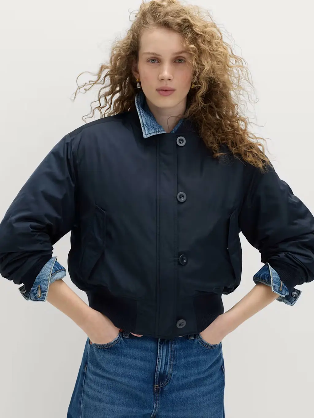 Woman wearing a navy bomber jacket over a denim shirt with jeans