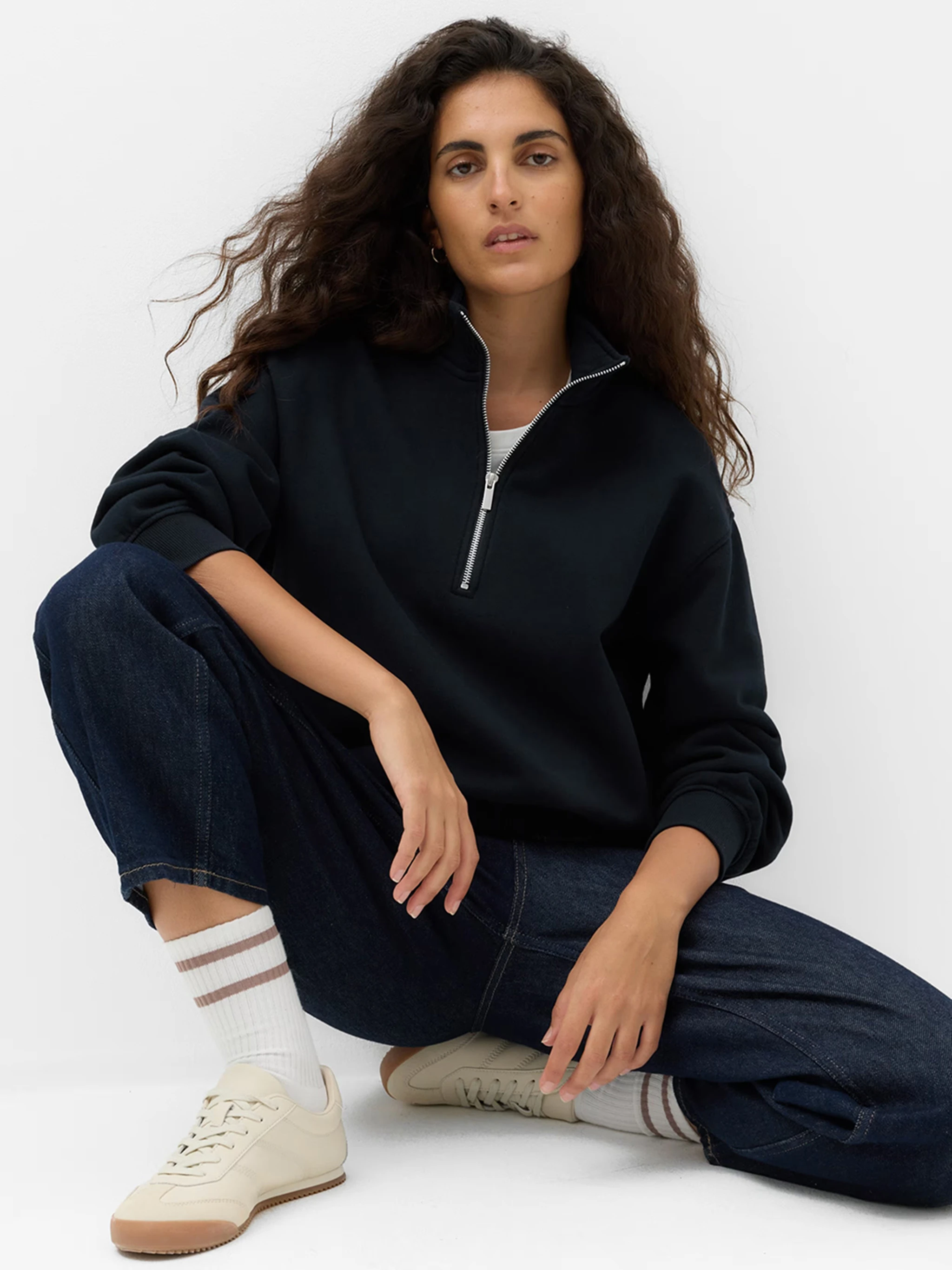 Woman wearing dark blue jeans and sweatshirt, ankle socks and beige trainers.
