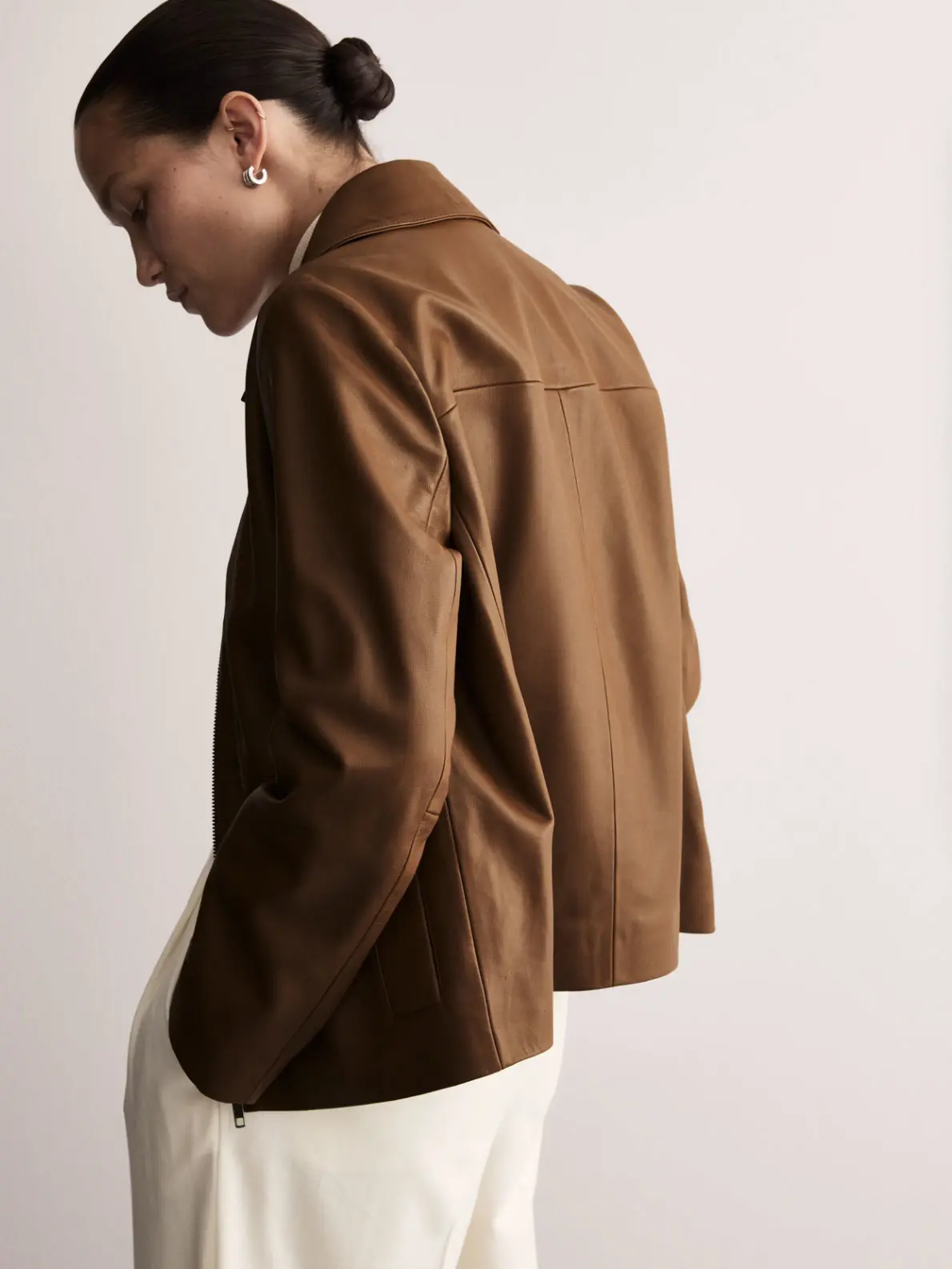 Woman wearing brown leather jacket and white trousers