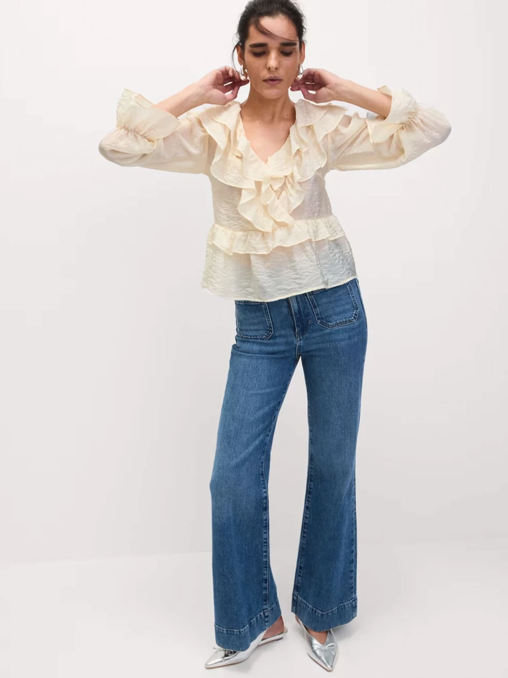 Woman wearing cream ruffled blouse and blue patch-pocket flared jeans