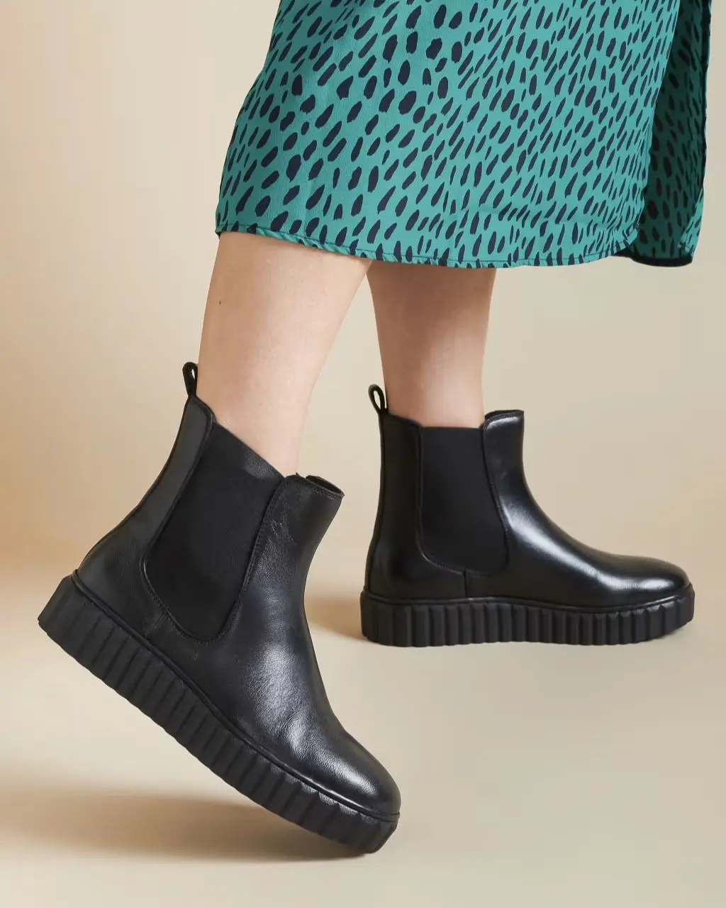 A close up of a woman wearing a black and green dress and platform Chelsea boots