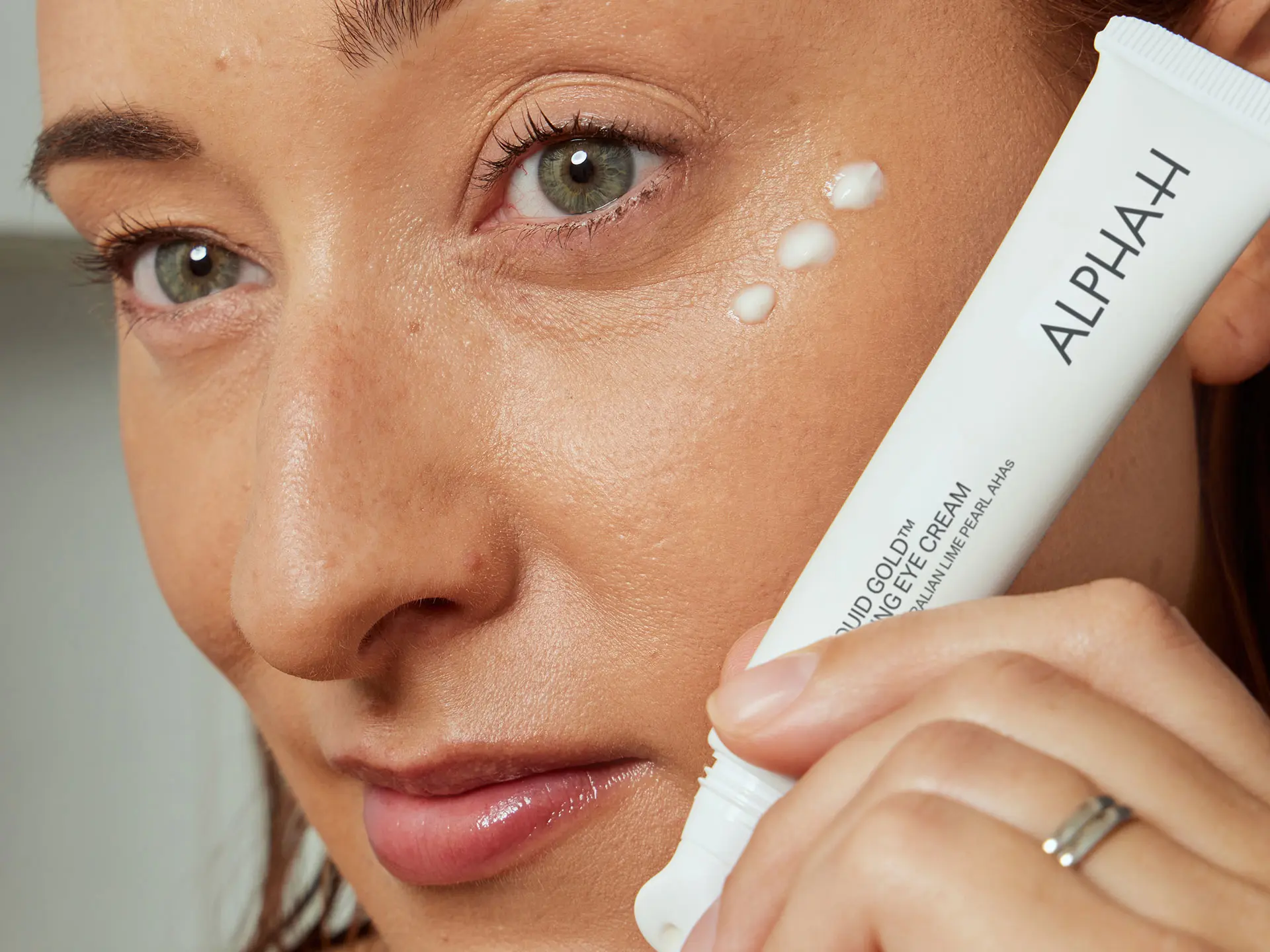 Woman holding an Alpha H eye cream against her cheek