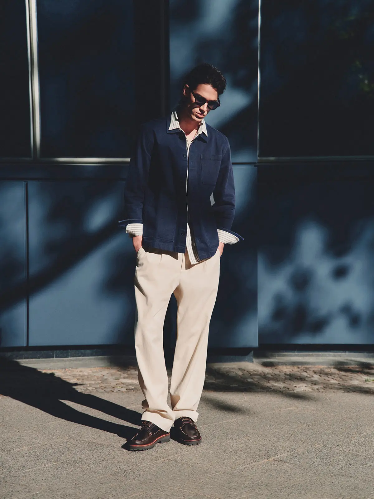 Man wearing navy shirt, neutral trousers, brown shoes and sunglasses 