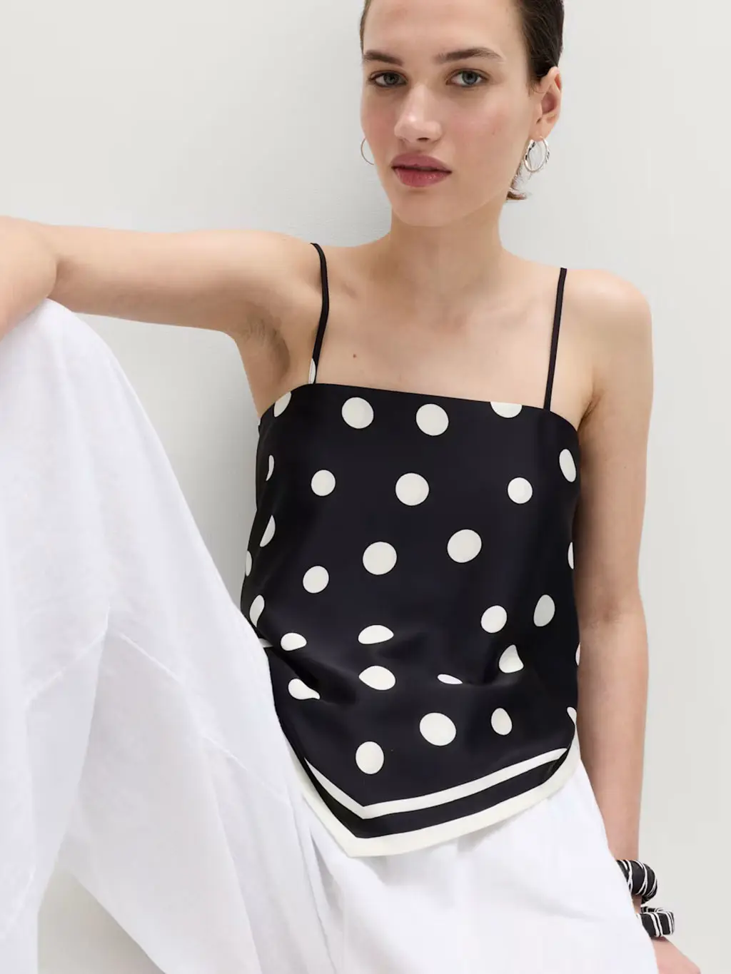 Woman wearing a polka-dot blouse with white linen trousers, silver hoop earrings and textured bangles