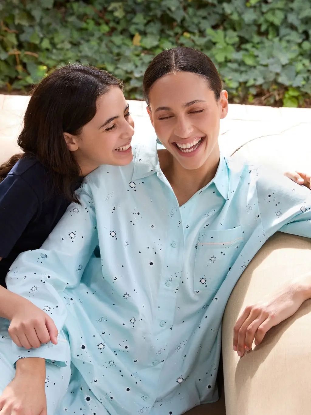 A woman wears light blue star pyjamas and is sat next to her daughter in navy blue pyjamas