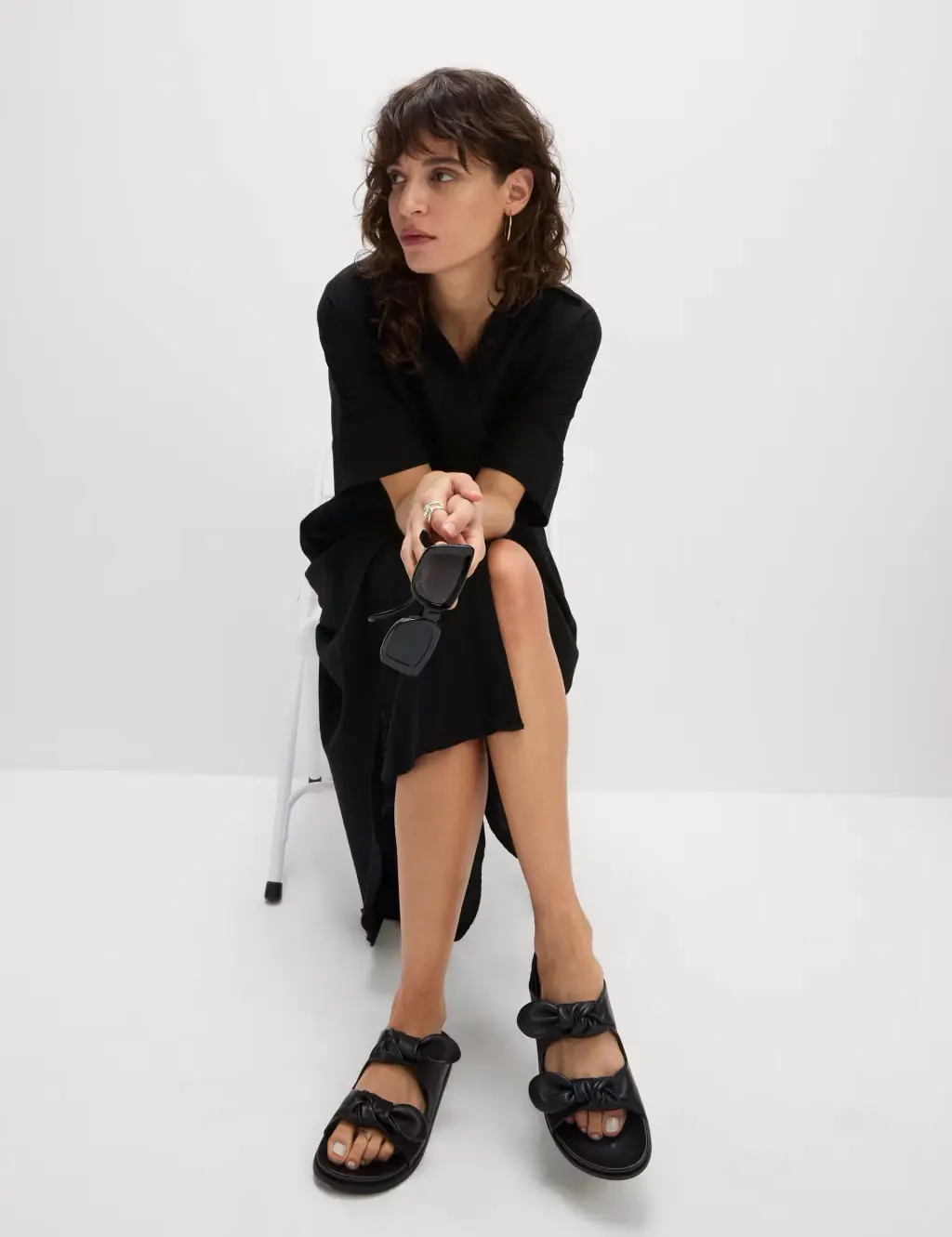 Woman wearing a black shirt dress, black sandals, gold earrings and black sunglasses