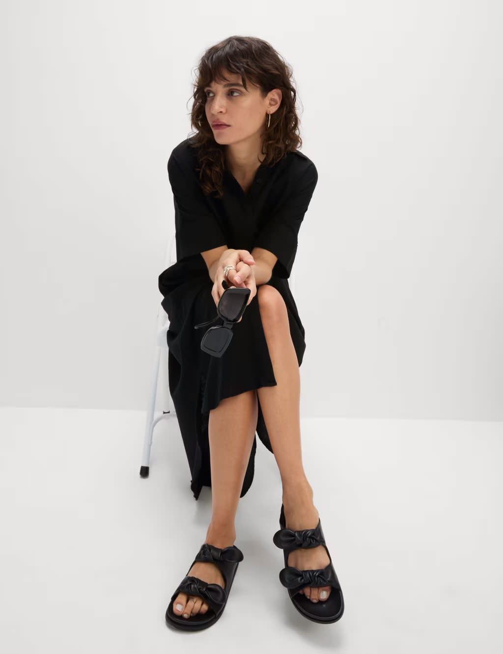 Woman wearing a black shirt dress, black sandals, gold earrings and black sunglasses