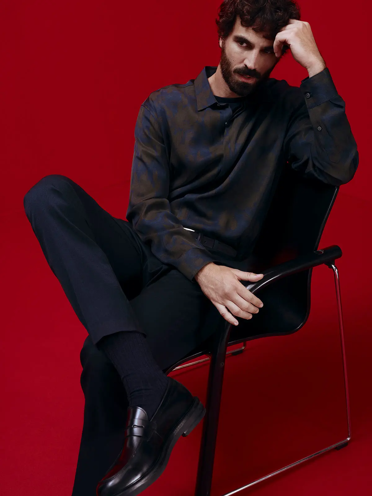 Man sitting on chair wearing abstract print shirt, smart navy trousers and formal shoes