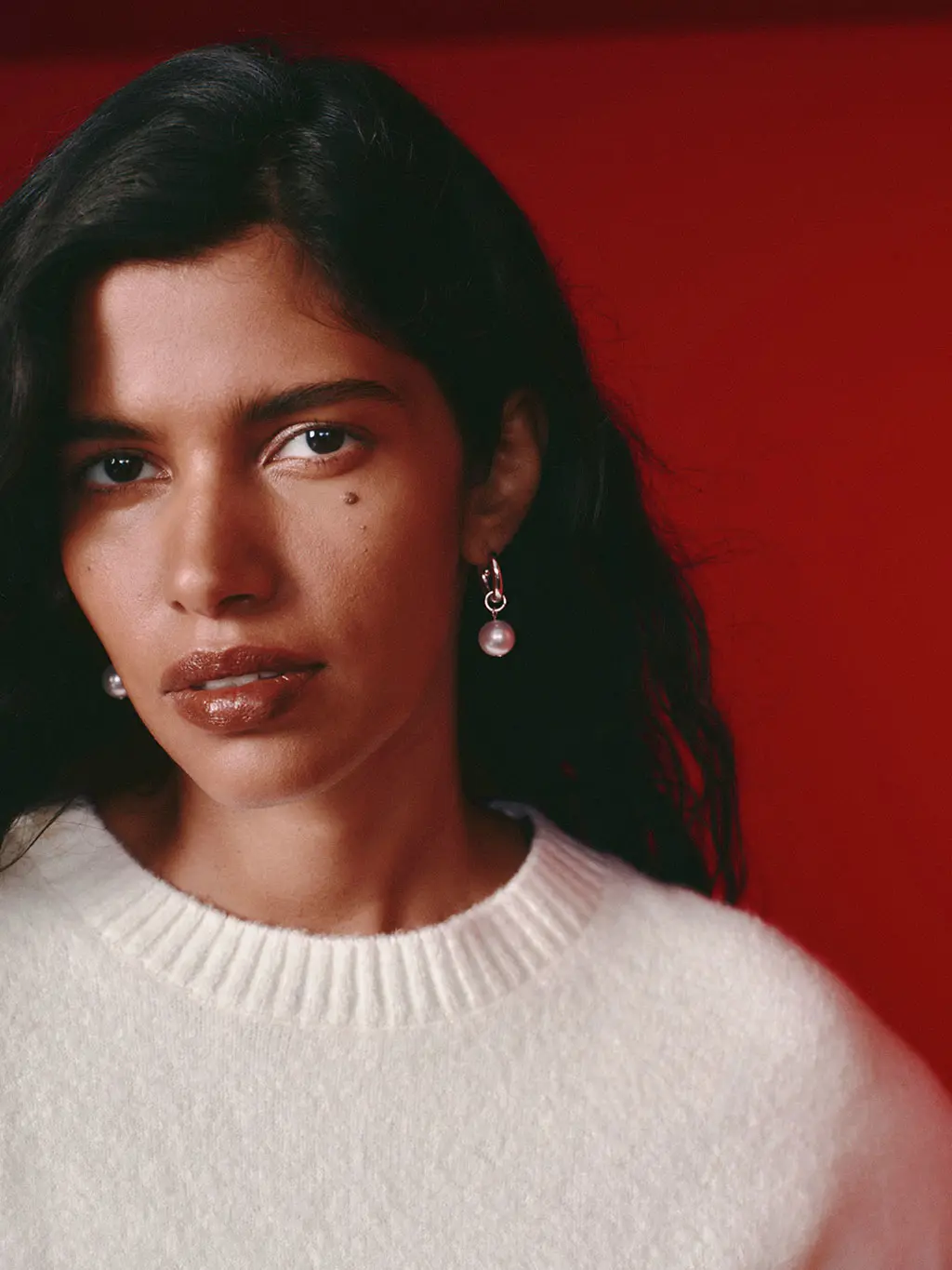 Woman wearing a cream jumper and pair of hoop earrings with a pearl pendant.